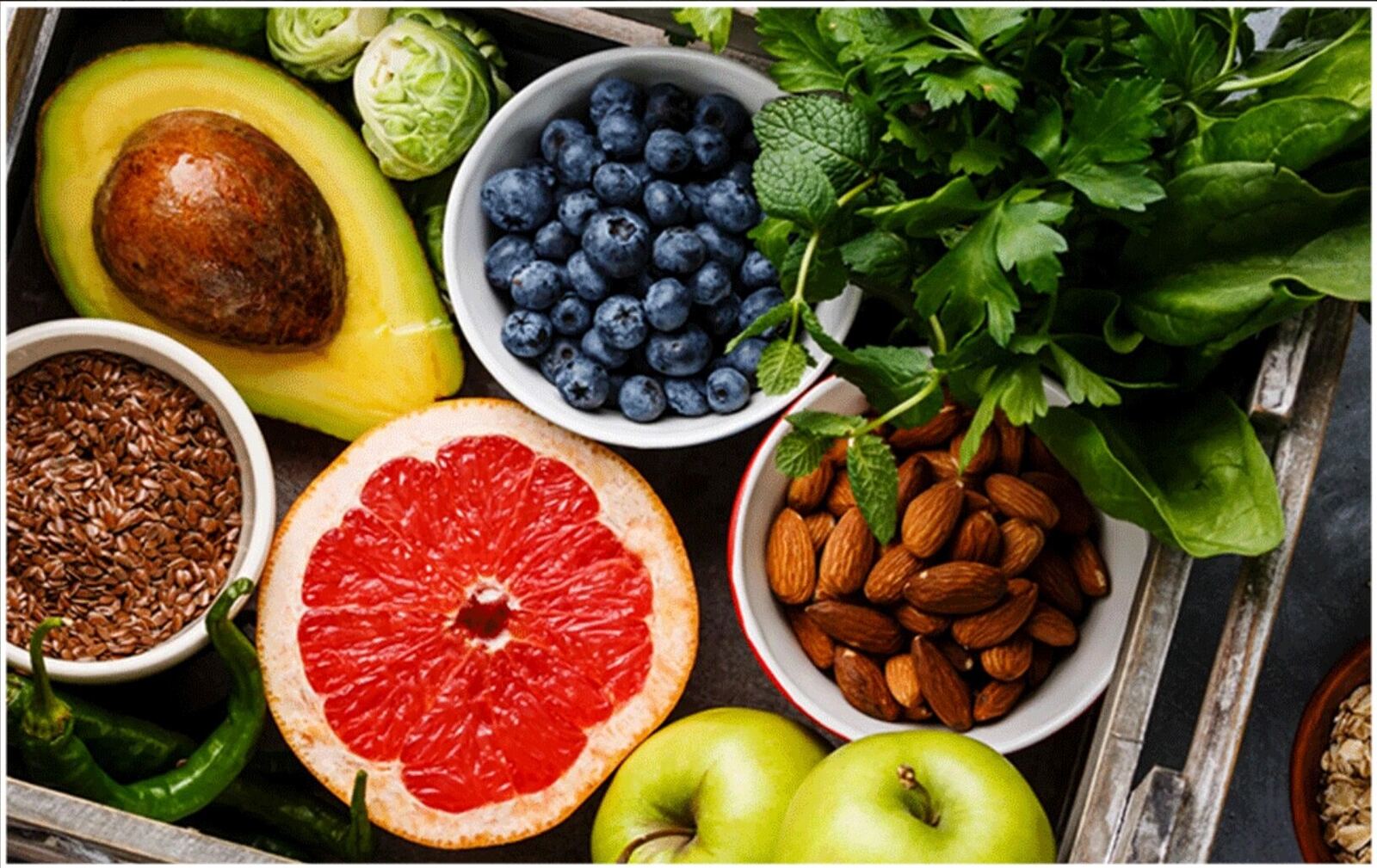 A wooden crate filled with avocado, blueberries, almonds, grapefruit and fresh greens